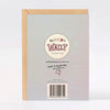 The back of a Wally Paper Co greeting card, shown with a kraft envelope behind it on a light grey background. The card back is pale lilac textured paper with printed branding, a barcode, and small text including 'Made in Melbourne, Australia'.