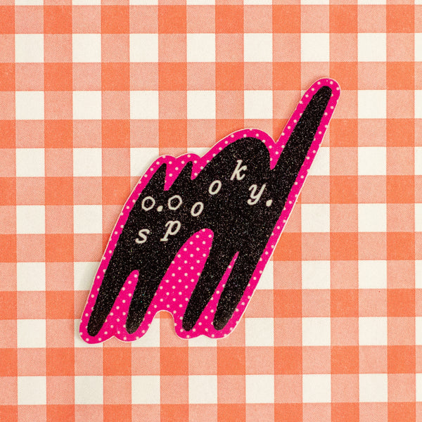 A die-cut sticker shaped like a cat silhouette, featuring a black glittery body with pink polka-dot accents and the words 'spooky.'