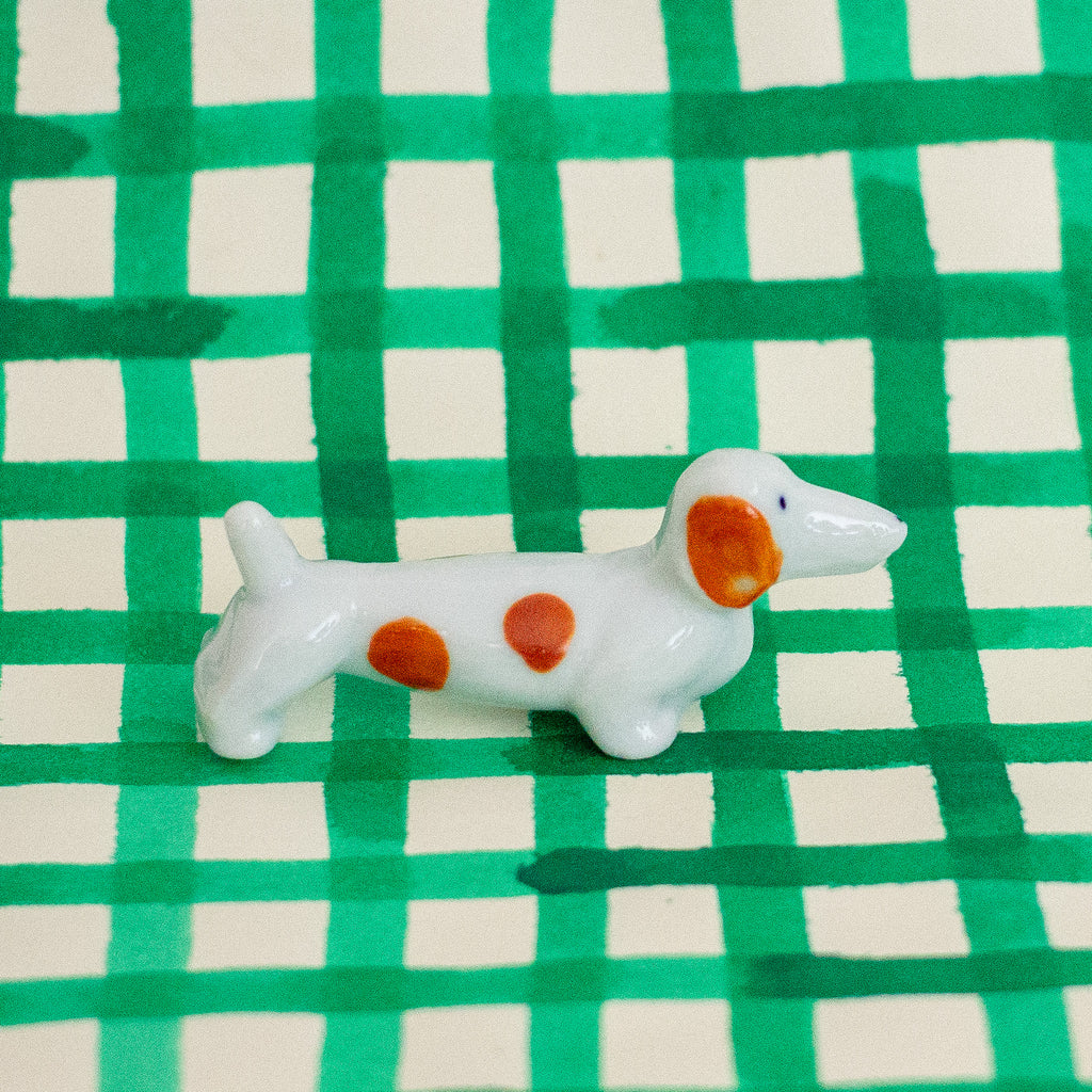 Small ceramic dog figurine with brown spots on a green and white checkered background
