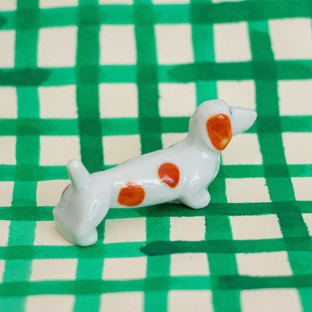Small ceramic dog figurine with brown spots on a green and white checkered background