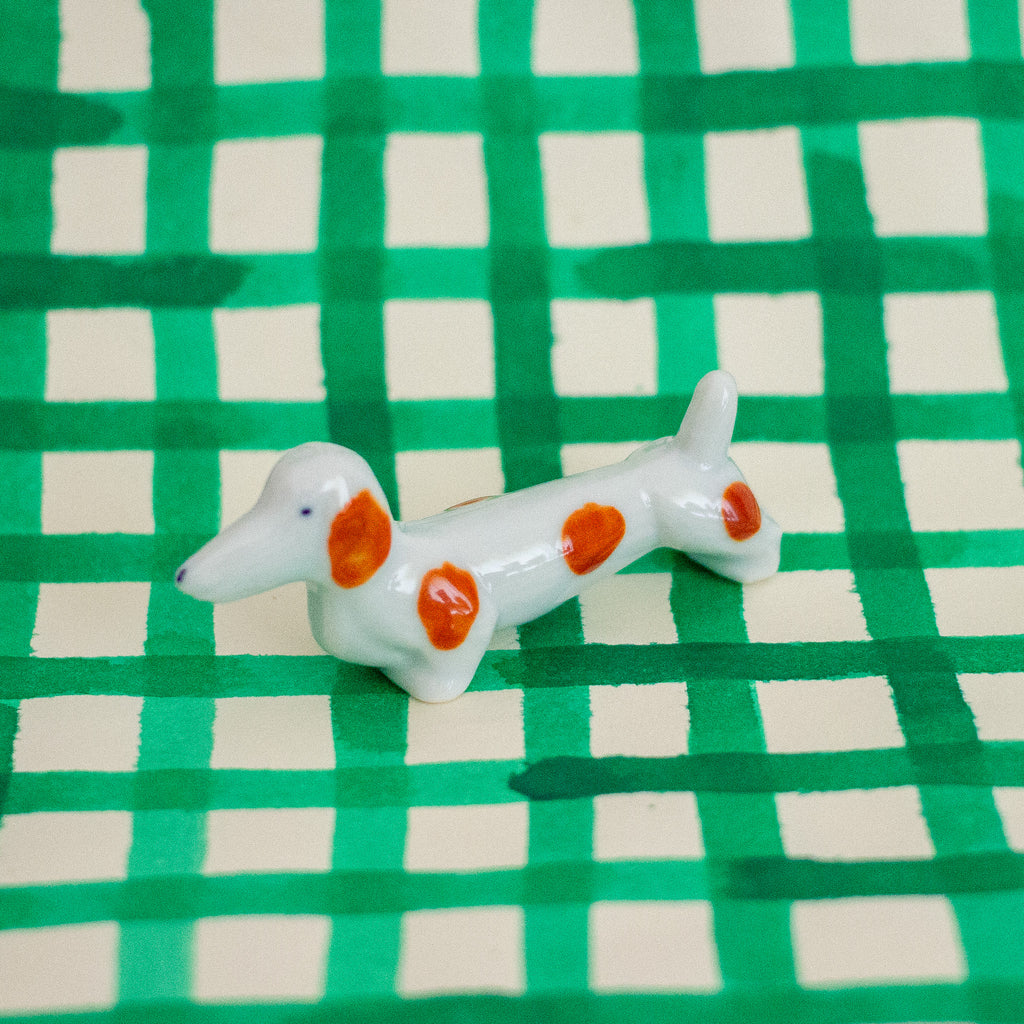 Small ceramic dog figurine with brown spots on a green and white checkered background