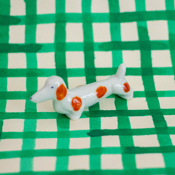Small ceramic dog figurine with brown spots on a green and white checkered background