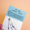 A hand holding a clear plastic package containing a white card with a black spotty dog illustration and a light blue paper header card that reads 'BY IMI PRINT SHOP' and 'Spotty Dog [GQCCO]'.