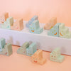A set of pastel-coloured ceramic trinket  with simple smiley faces, arranged on a white platform and a peach-coloured surface.