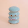 Light blue ceramic smiley face figurine on a peach background
