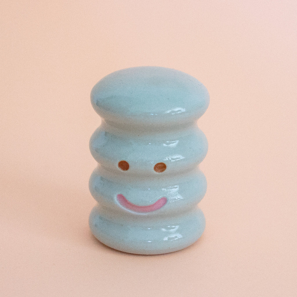 Light blue ceramic smiley face figurine on a peach background