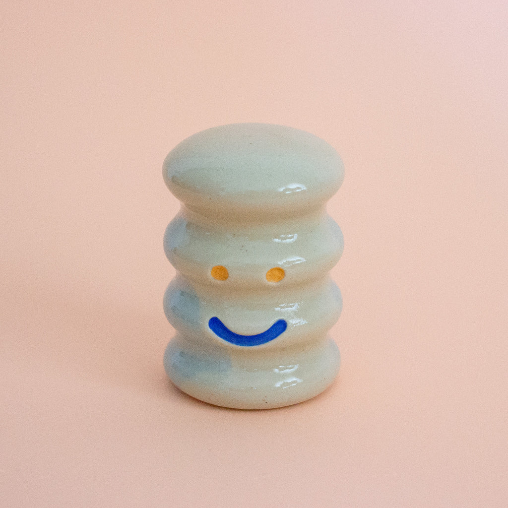 Small ceramic figurine with a smiley face on a peach background