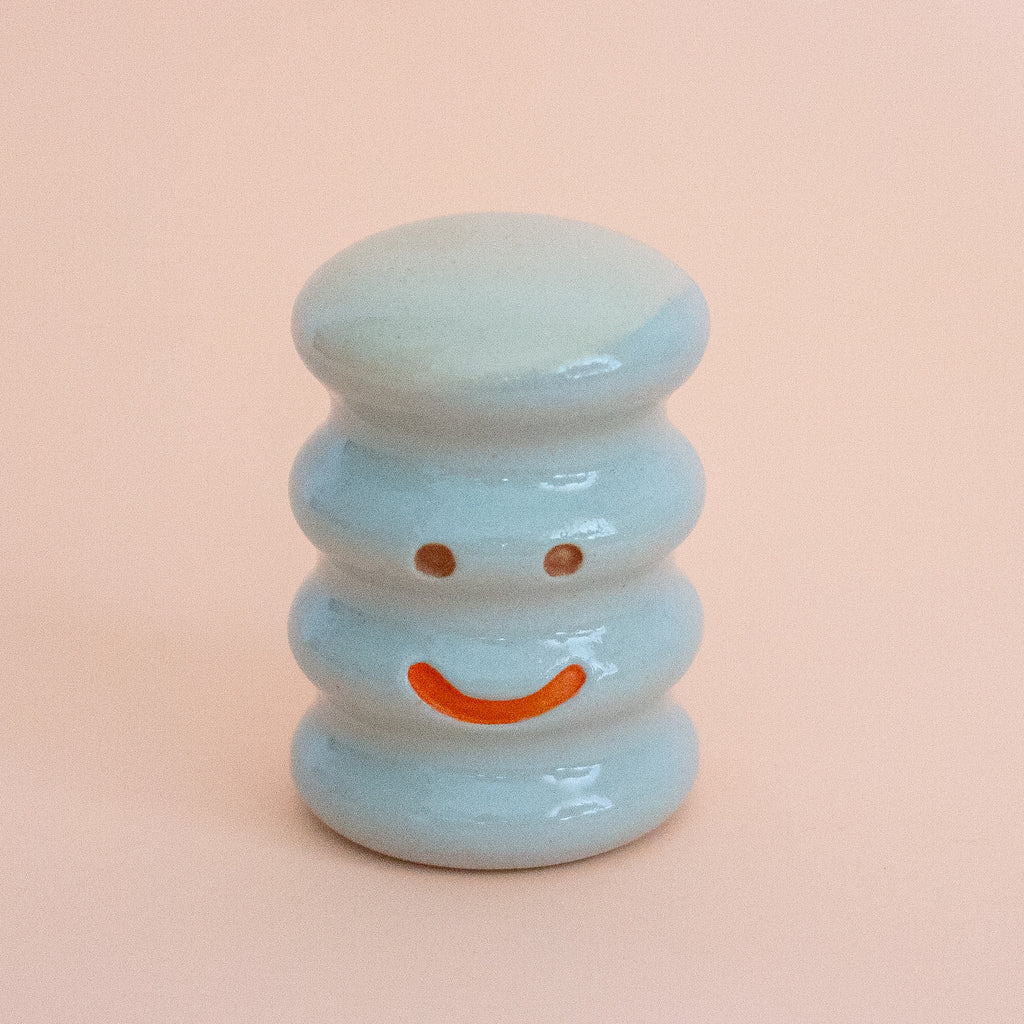 Small ceramic figurine with a smiley face on a peach background
