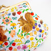 A close-up of a white kiss-lock clutch bag decorated with a colourful print featuring two brown squirrels, red fruits, purple berries, and yellow flowers. The bag has a gold-tone metal frame and is photographed on a clean white background.