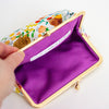 An open kiss-lock clutch purse with a white floral fabric exterior, a gold-tone metal frame, and a bright purple cotton interior. A hand is holding the left side of the purse, and a white interior label is visible.