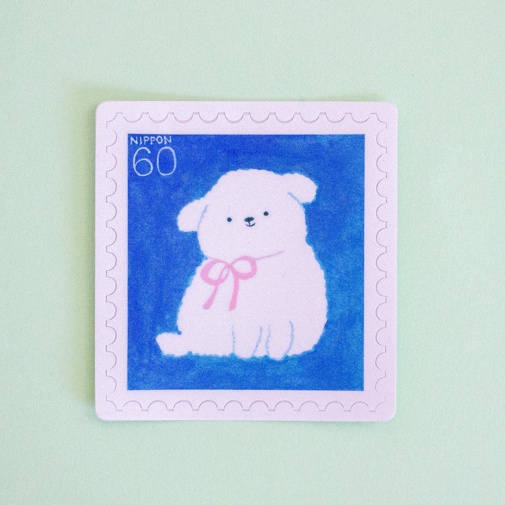 A square postage stamp design featuring a white fluffy puppy wearing a pink bow on a blue background, with a light pink border and the text 'NIPPON 60' in the top left, shown on a pale mint green background.