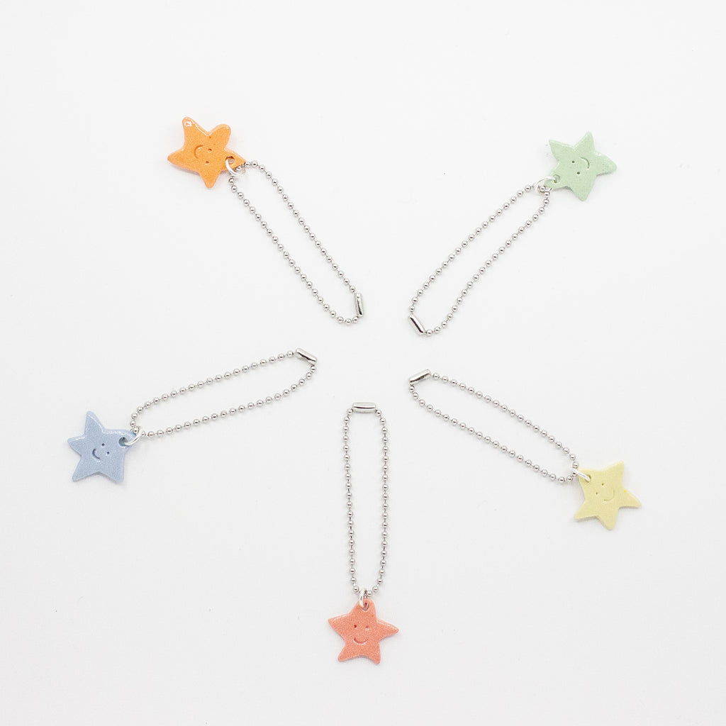 Colorful star-shaped bag charms on chains arranged in a circle on a white background.