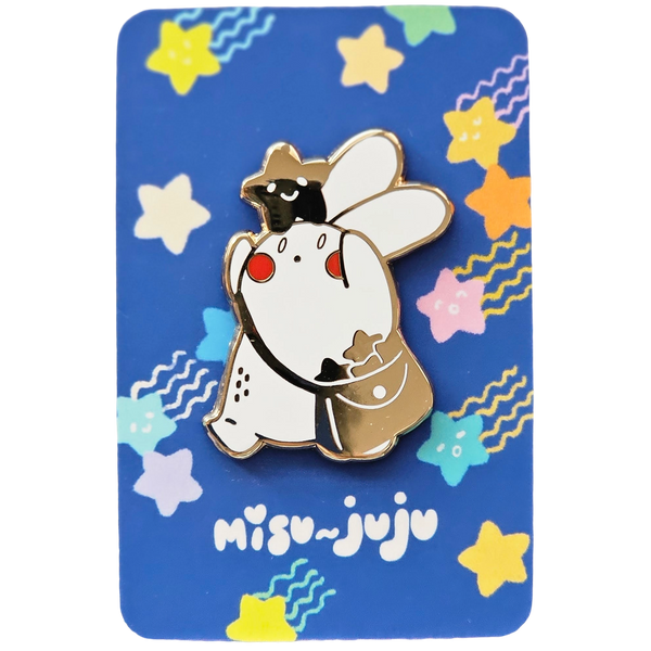 A Misu Juju enamel pin of the bunny character wearing a star on its head and bag, mounted on a blue backing card decorated with colourful stars and the Misu Juju logo.