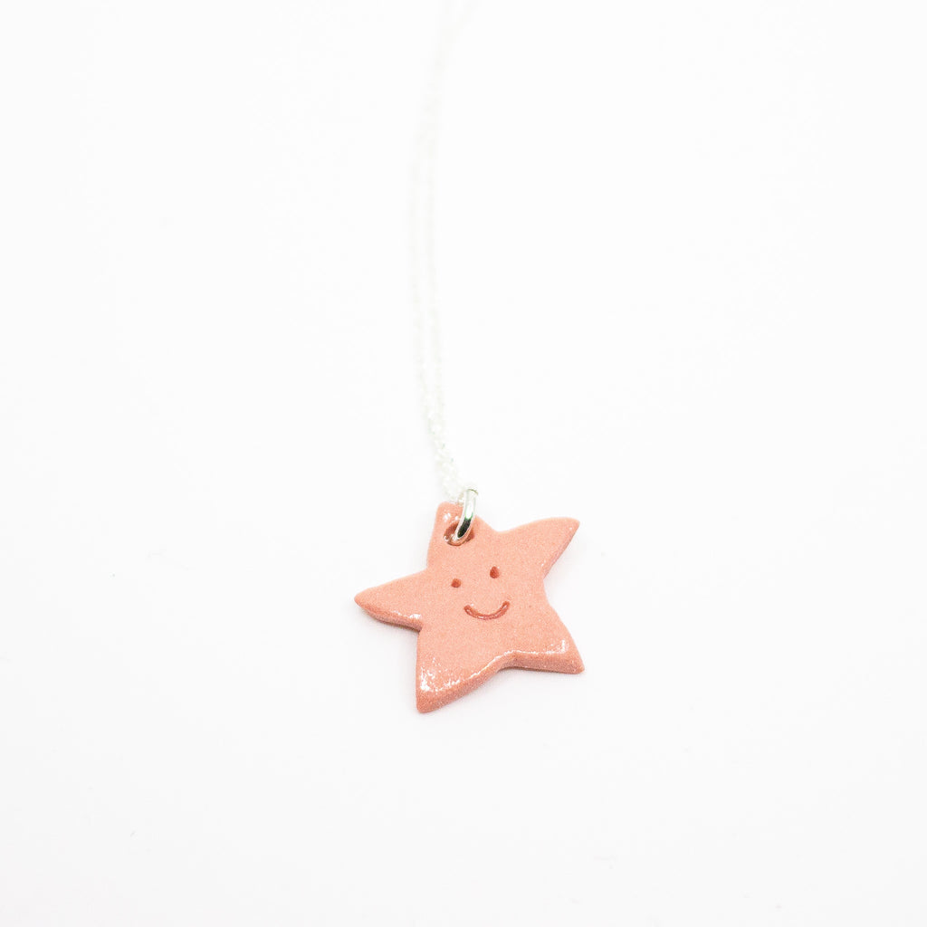 Pink star-shaped pendant with a smile on a white background