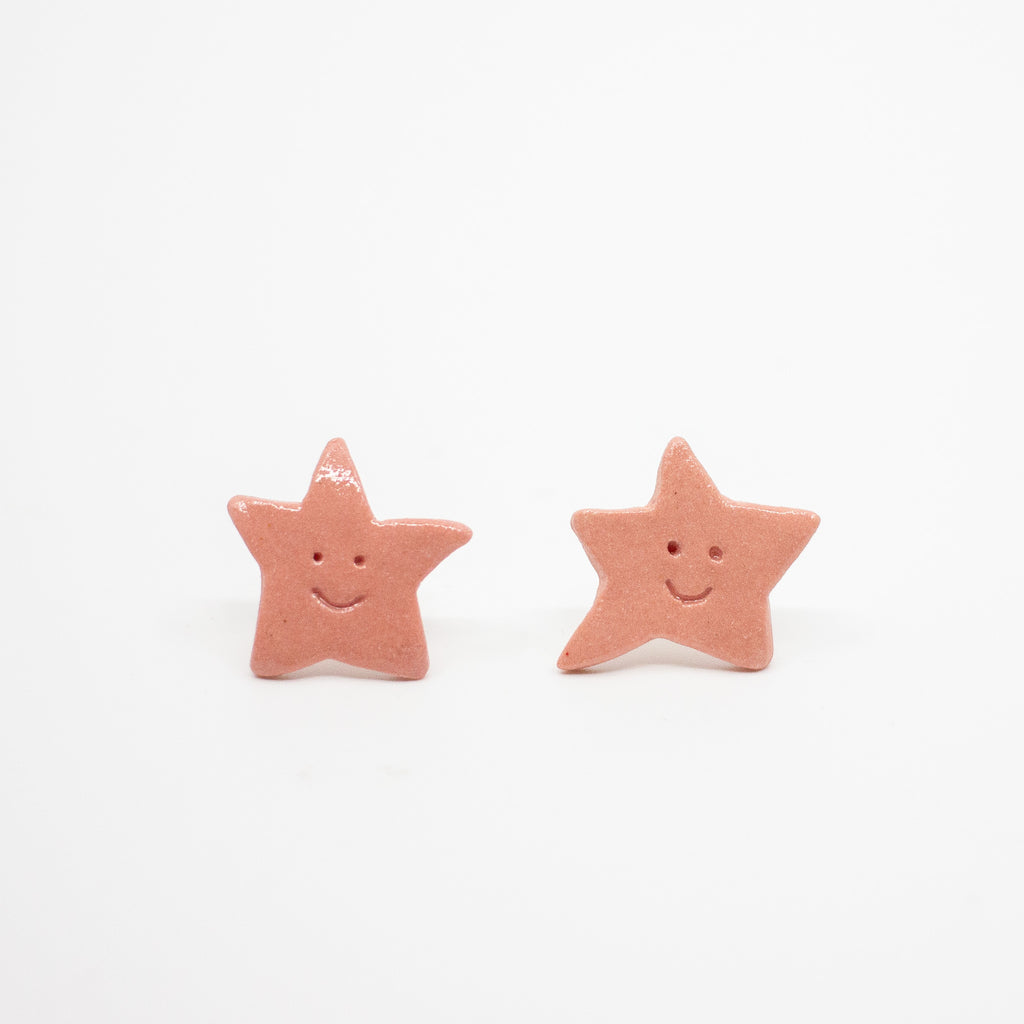 Pair of Rose Pink star-shaped earrings with smiling faces on a white background