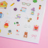 A sheet of colourful stationery stickers displayed on a solid pink background. The sticker sheet contains various cute illustrations of pens, notebooks, flowers, and office items.