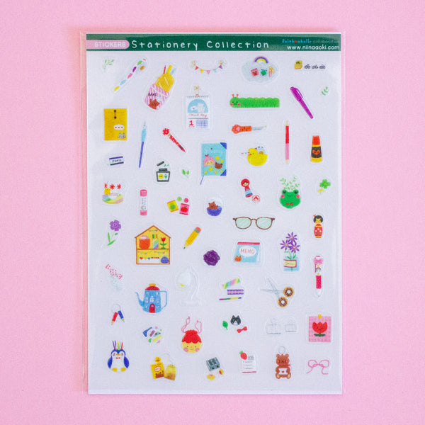 A sheet of colourful stationery stickers displayed on a solid pink background. The sticker sheet contains various cute illustrations of pens, notebooks, flowers, and office items.