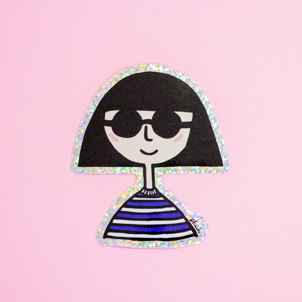 A die-cut sticker featuring a girl with bob hair wearing sunglasses shaped character with a holographic border, set against a plain pink background.