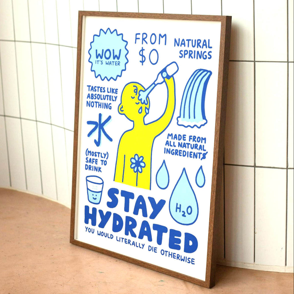 A framed educational poster titled 'STAY HYDRATED' leaning against a white tiled wall on a wooden surface. The poster features a yellow cartoon figure drinking water, blue text, and water droplet illustrations.