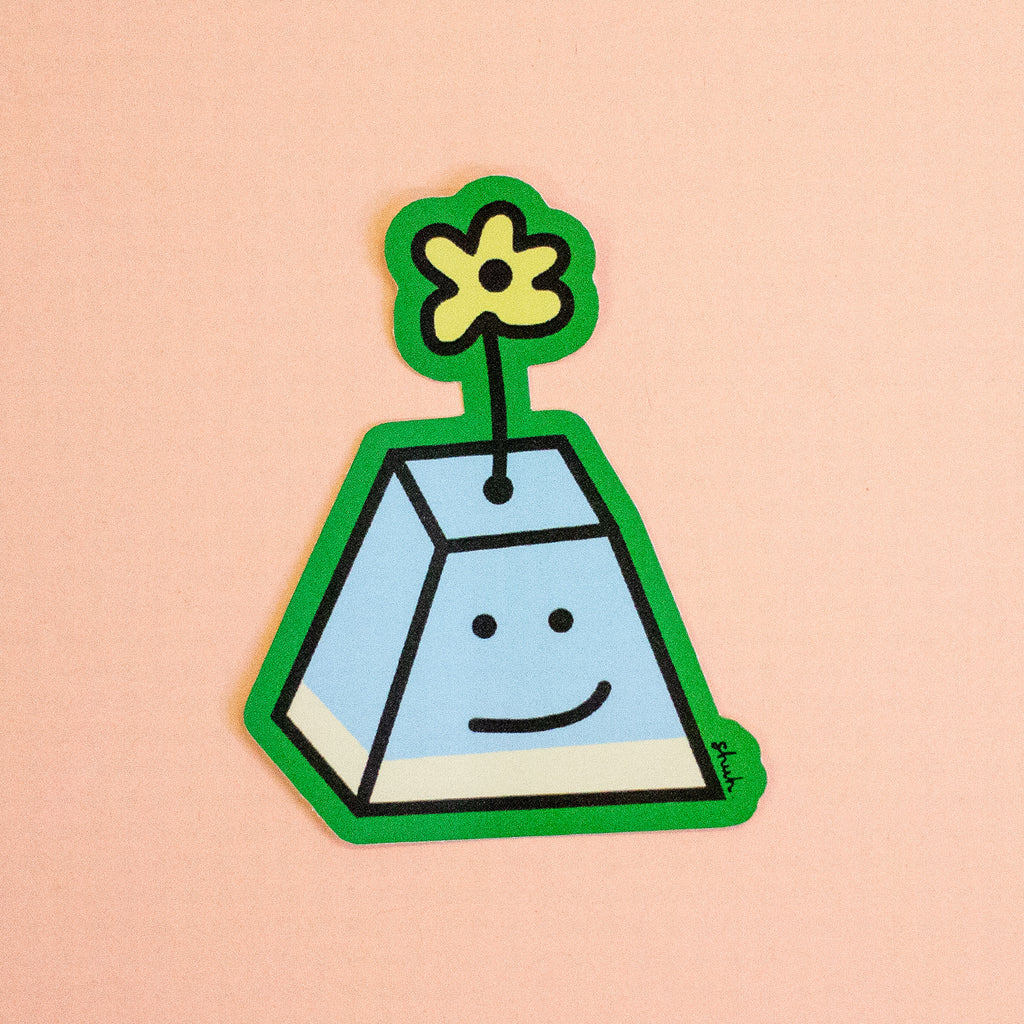 A die-cut sticker featuring a cute, smiling A-shaped character with a green border, light blue body, and a yellow flower on top, set against a solid peach background.