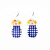 Closeup photo of the still life earrings with sterling silver hooks. Ceramic beads are vase shaped, with blue checkered pattern. Hand painted flowers are arranged at the top of the vase. 