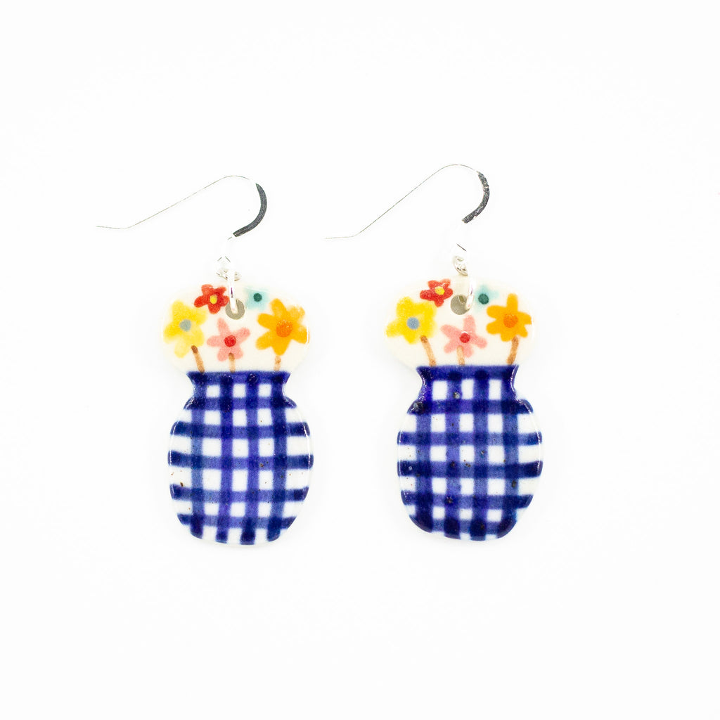 Closeup photo of the still life earrings with sterling silver hooks. Ceramic beads are vase shaped, with blue checkered pattern. Hand painted flowers are arranged at the top of the vase. 