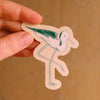 A hand holding an illustrated sticker of a stilt with a beige outline.