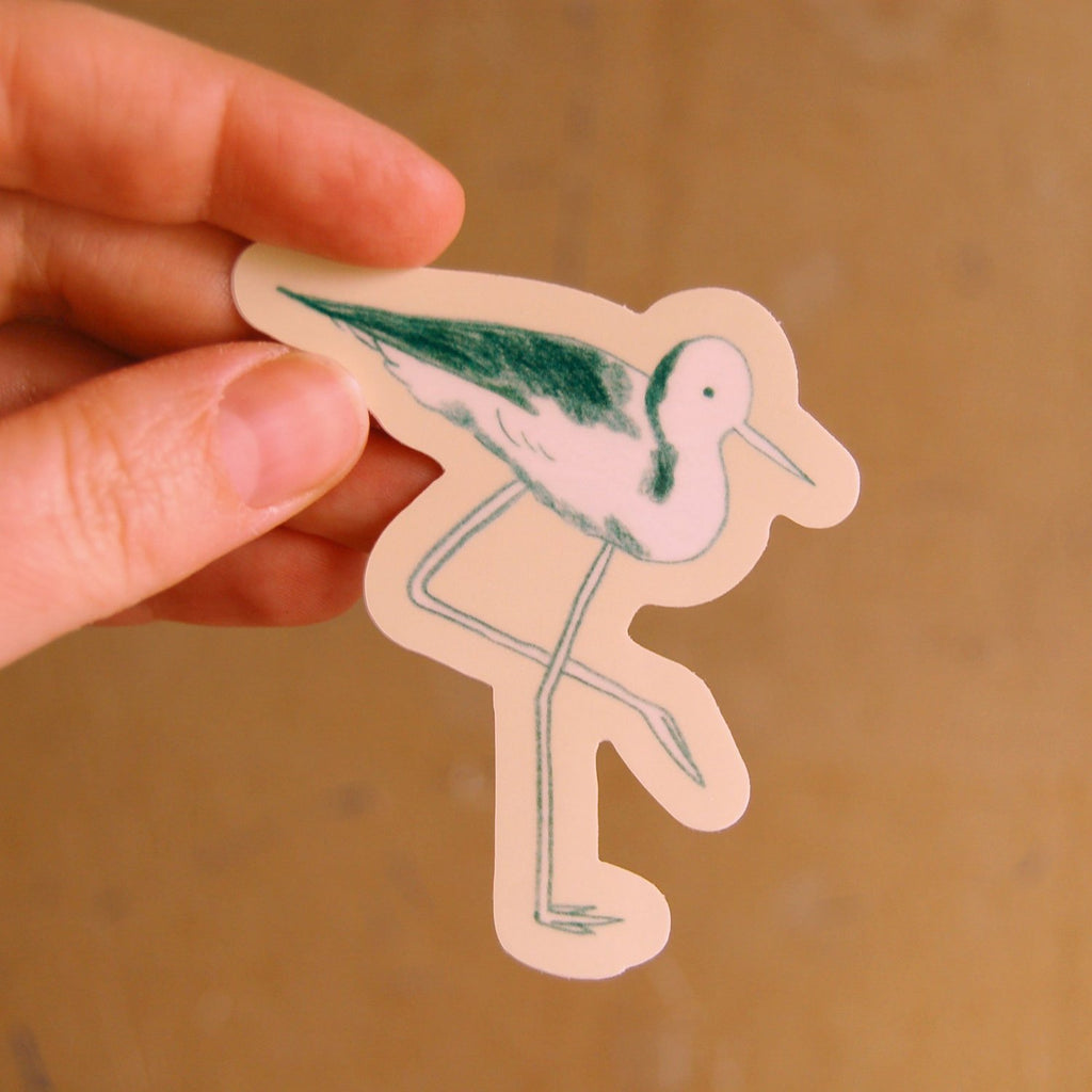 A hand holding an illustrated sticker of a stilt with a beige outline.