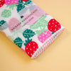 A folded Japanese handkerchief with a strawberry and leaf pattern, featuring a clear paper band label that reads 'HAIKARA HANDKERCHIEF made in JAPAN', set against a solid pale yellow background.