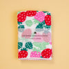 A folded Japanese handkerchief with a strawberry and leaf pattern, featuring a clear paper band label that reads 'HAIKARA HANDKERCHIEF made in JAPAN', set against a solid pale yellow background.