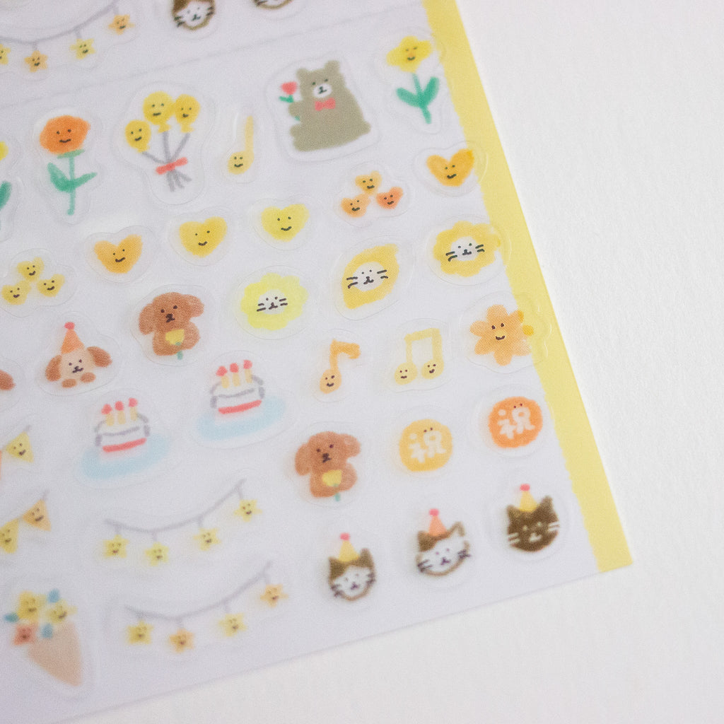 A close-up of a sheet of cute cartoon stickers on a white background, featuring small yellow smiley faces, flowers, animals, and birthday-themed icons, with a yellow border along the right edge.