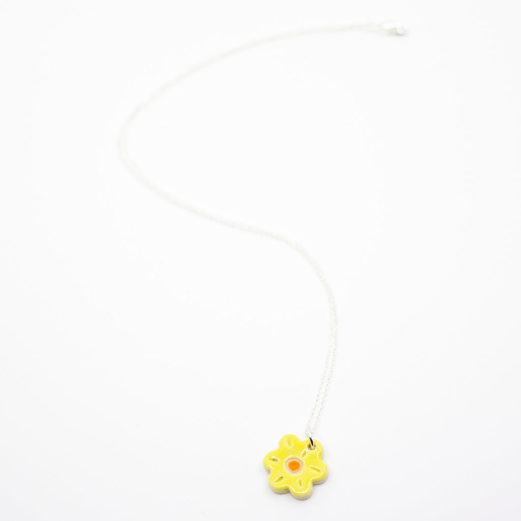 Yellow flower-shaped pendant on a white chain against a white background