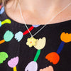 A close-up of a person wearing a delicate silver chain necklace with a small yellow flower pendant, styled over a black top with a colourful tulip pattern.