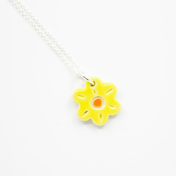 Yellow flower-shaped pendant on a silver chain against a white background