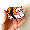 Hand holding a patch of sushi with a cat design on a plain background
