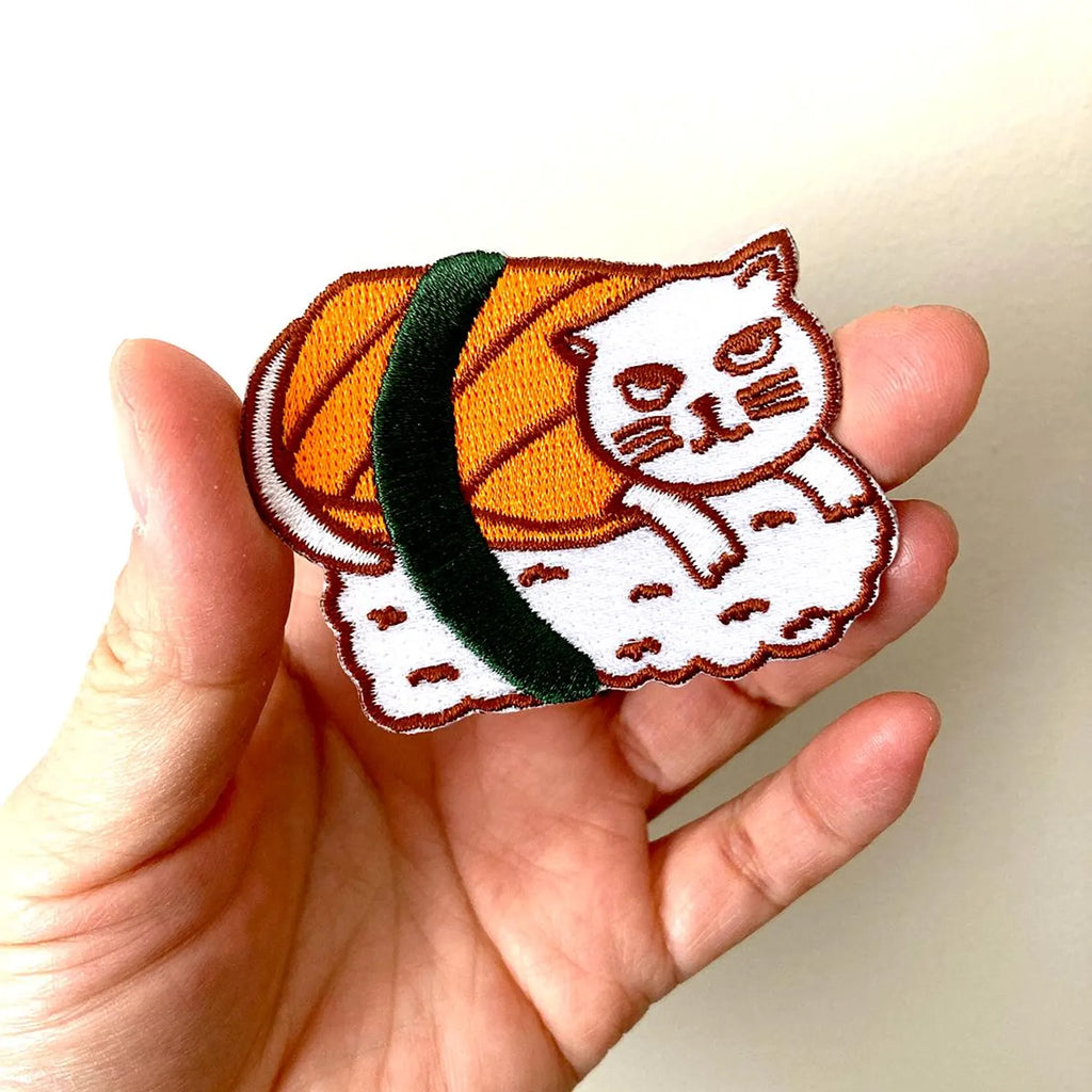 Hand holding a patch of sushi with a cat design on a plain background