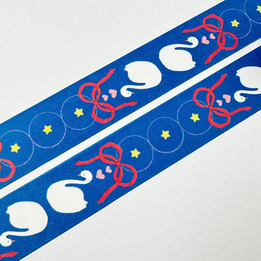 A close-up of a blue decorative strip with repeating white swan motifs, red ribbon bows, yellow stars, and small pink hearts on a white background.