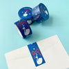 Three rolls of decorative washi tape with a blue, red, and white swan design are arranged on a light blue background next to a white envelope featuring a matching blue label.