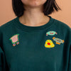 Green sweatshirt with colorful embroidered designs on a peach background
