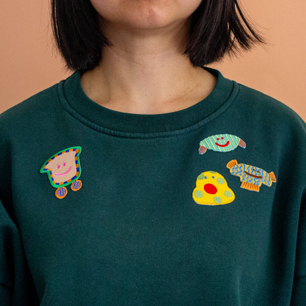 Green sweatshirt with colorful embroidered designs on a peach background