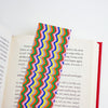 A colourful wavy stripe pattern bookmark with pink, orange, brown, yellow, grey, green, and blue,  shown resting on an open book against a plain white background.