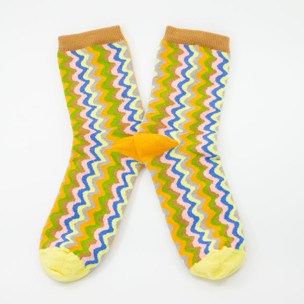 Pair of colourful zigzag-patterned crew socks featuring yellow, green, pink, blue, and brown tones with yellow toes and brown cuffs.