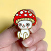 Hand holding a cute cartoon mushroom-shaped pin against a yellow background