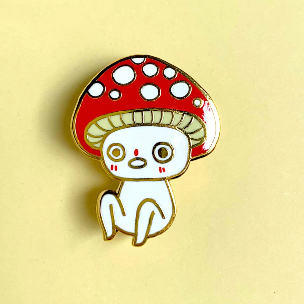 Enamel pin with a cartoon cat under a red mushroom on a beige background