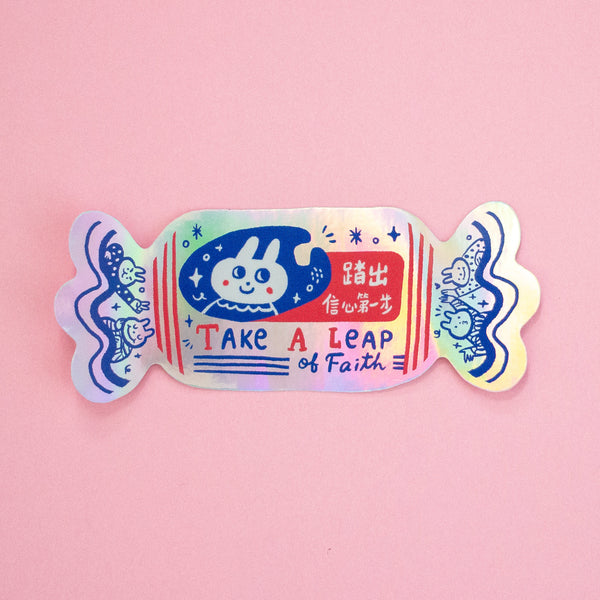 A holographic sticker in a shape of a candy with 'Take A Leap of Faith' text. 