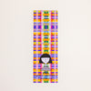 A rectangular postcard featuring a colourful plaid print with a girl logo on the bottom on a off-white background. 