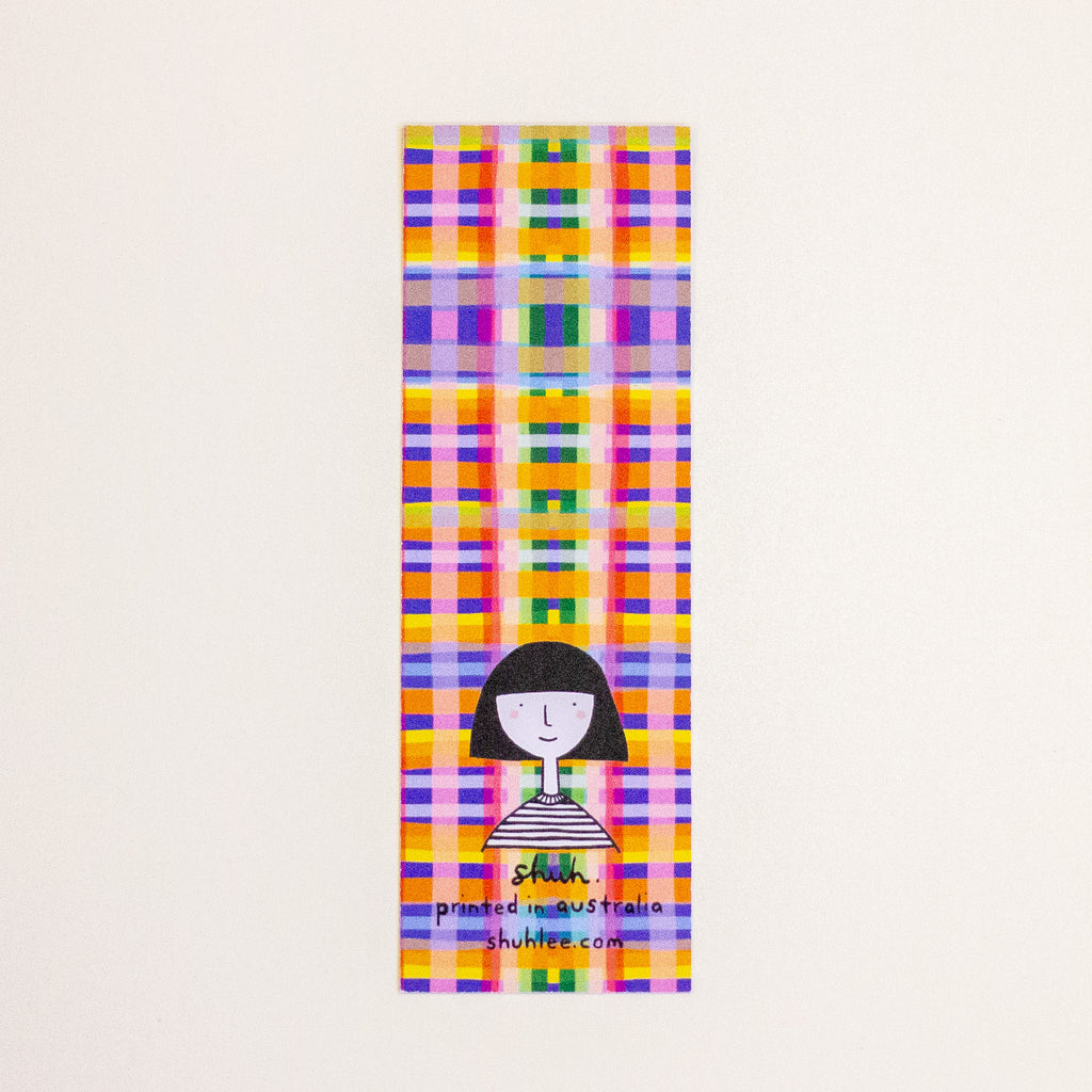 A rectangular postcard featuring a colourful plaid print with a girl logo on the bottom on a off-white background. 