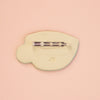 A pale yellow brooch with a silver-tone metal pin bar, shown from the back on a solid peach background. 