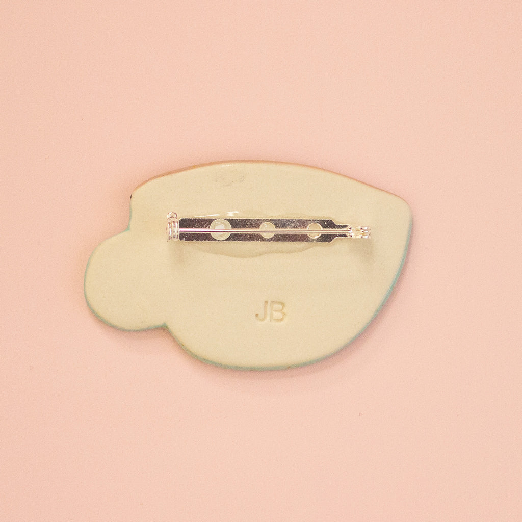 A pale yellow brooch with a silver-tone metal pin bar, shown from the back on a solid peach background. 