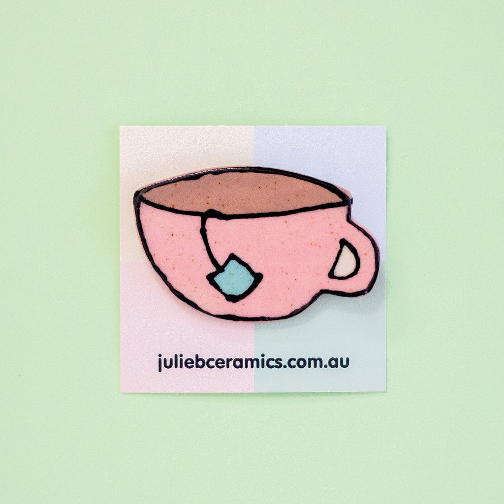 A pink teacup brooch on a square card  on a mint background.